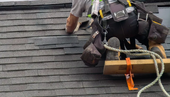 Roofer performing shingle roof replacement with tools.